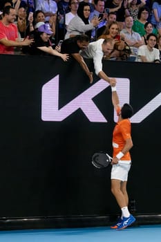 MELBOURNE, AUSTRALIA - JANUARY 13: Novak Djokovic of Serbia celebrates a point against Nick Kyrgios of Australia with a fan in an Arena Showdown charity match ahead of the 2023 Australian Open at Melbourne Park on January 13, 2023 in Melbourne, Australia.