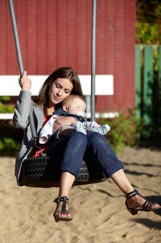 Hes a big responsibility. Young mom on a park swing with her baby boy