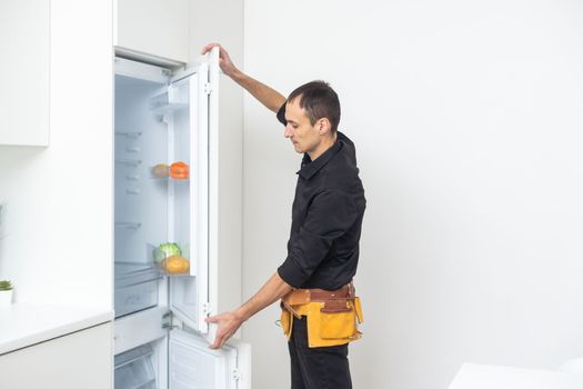 Young Male Repairman Fixing Refrigerator In Kitchen.