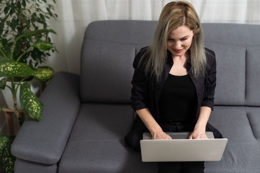 Smiling young woman using laptop, sitting on couch at home, beautiful girl shopping or chatting online in social network, having fun, watching movie, freelancer working on computer project