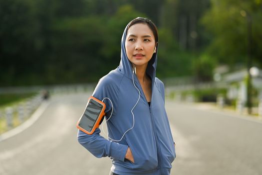 Young asian woman in sportswear listening to music in earphone walking in the park. Healthy lifestyle, workout and wellness concept.