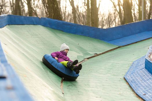 Active girl sliding down the hill on snow tube. Cute little happy child having fun outdoors in winter on sledge . Healthy excited kid tubing snowy downhill, family winter time.