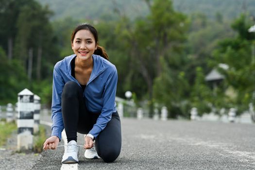 Smiling sportswoman tying shoelaces before running, getting ready for jogging outdoors. Healthy lifestyle concept.