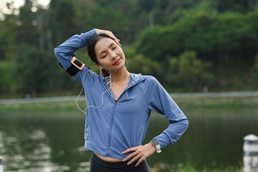 Beautiful woman stretching arms and breathing fresh air while exercising in the park. Sport and healthy lifestyle concept.
