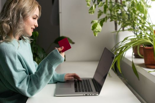 Young woman holding credit card and using laptop computer. Businesswoman or entrepreneur working at home. Online shopping, e-commerce, internet banking, spending money, working from home concept