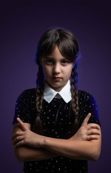 Portrait of little girl with Wednesday Addams costume during Halloween. Serious expression and dark atmosphere with dark background