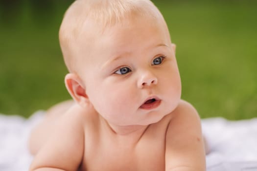 Cute happy toddler lying on a blanket on the grass outdoors in summer.