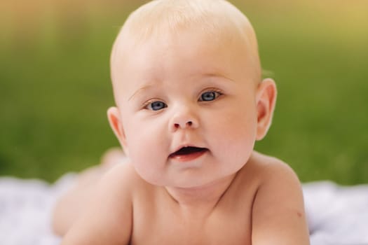 Cute happy toddler lying on a blanket on the grass outdoors in summer.