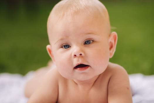 Cute happy toddler lying on a blanket on the grass outdoors in summer.