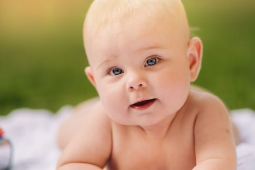 Cute happy toddler lying on a blanket on the grass outdoors in summer.