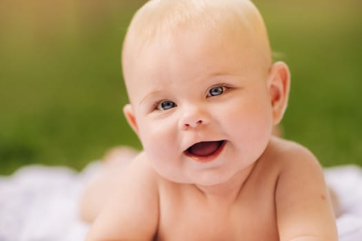 Cute happy toddler lying on a blanket on the grass outdoors in summer.