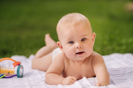 Cute happy toddler lying on a blanket on the grass outdoors in summer.