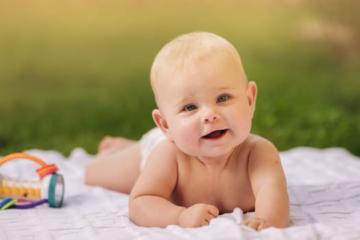 Cute happy toddler lying on a blanket on the grass outdoors in summer.