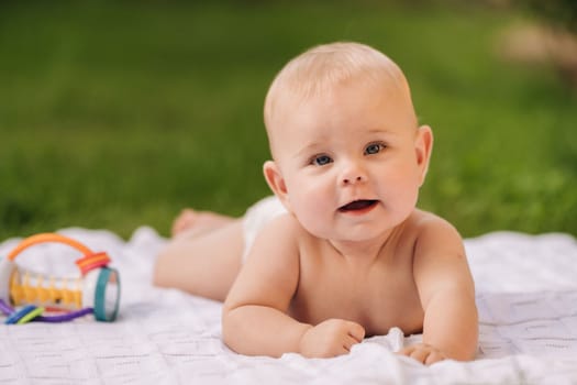 Cute happy toddler lying on a blanket on the grass outdoors in summer.