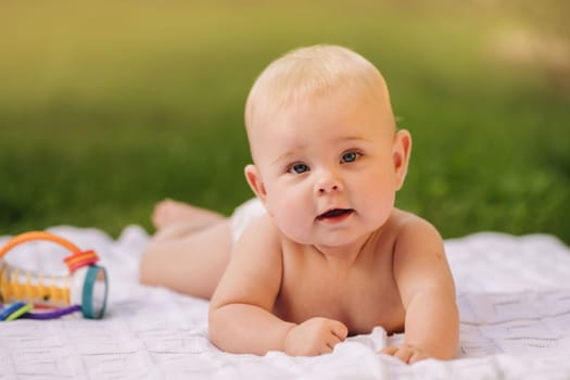 Cute happy toddler lying on a blanket on the grass outdoors in summer.