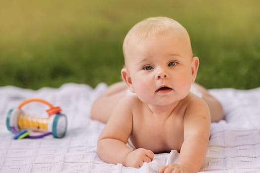 Cute happy toddler lying on a blanket on the grass outdoors in summer.