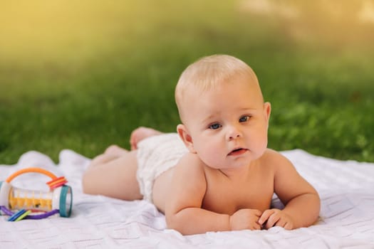 Cute happy toddler lying on a blanket on the grass outdoors in summer.