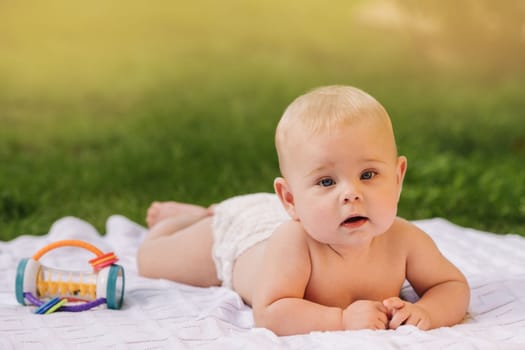 Cute happy toddler lying on a blanket on the grass outdoors in summer.