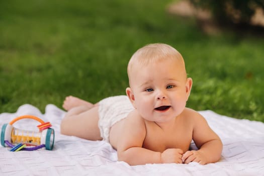 Cute happy toddler lying on a blanket on the grass outdoors in summer.