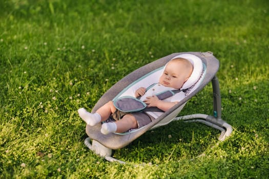 Cute happy toddler Sitting in a chair on the grass outdoors in summer.