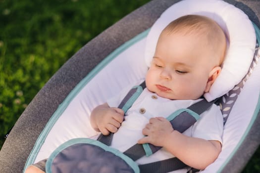 Cute happy toddler Sitting in a chair on the grass outdoors in summer.