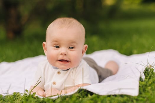 Cute happy toddler lying on a blanket on the grass outdoors in summer.