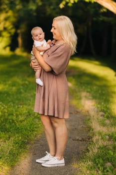 A mother holds a happy baby boy in her arms in a summer park.