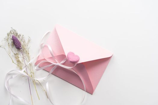 Minimal composition with a pink envelope, white blank card and a wax flower on a white background. Mockup with envelope and blank card. Flat lay. Top view