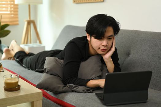 Casual man lying on couch and using computer tablet.