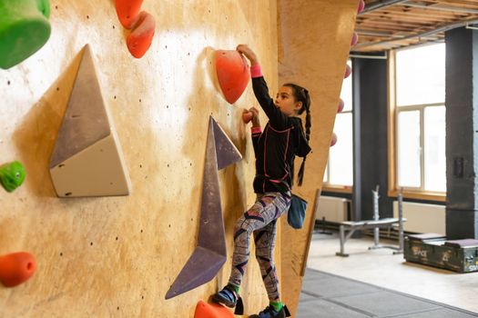 Junior Climber Girl shirt hanging on holds on climbing wall of indoor gym.