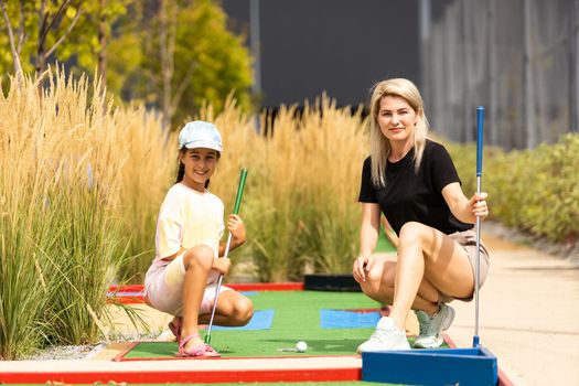 Detail of young woman and daughter playing mini adventure golf on a beautiful sunny summer day.