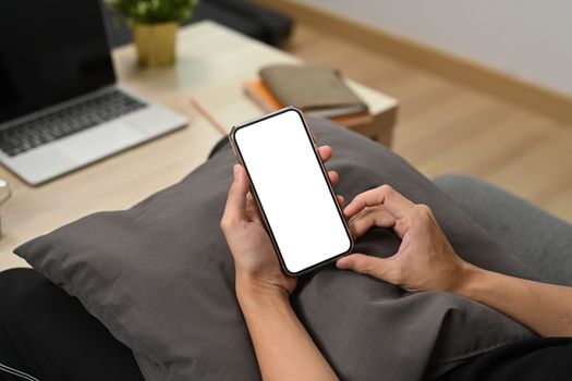 Close up view man holding smart phone while sitting on couch.