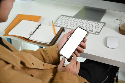 Cropped shot man using smart phone while sitting at his workplace.