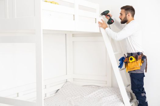 worker with screwdriver assembles and installs furniture in the children's room.