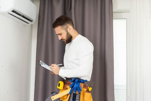 Young Technician using digital tablet and pen checking air conditioner in house room. Air Conditioning system installation and repairing concept.