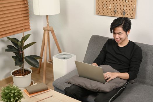 Young man surfing internet with laptop on sofa.