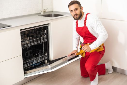 Young Repairman Service Worker Repairing Dishwasher Appliance In Kitchen.