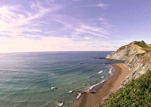 Panoramic view of Zumaya beach in Spain. no people, sand, sunny sky with clouds, gentle waves, rocky formations, cliffs. Flysch