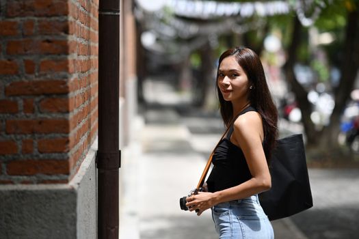 Asian woman traveler holding her digital camera and walking down the city street.