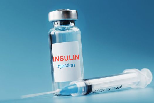 A bottle of insulin hormone and a syringe on the table on a blue background