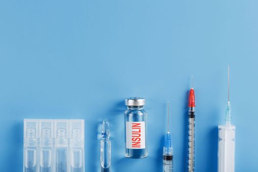 Ampoule bottle with insulin, needles and syringes for medical subcutaneous injection on a blue background