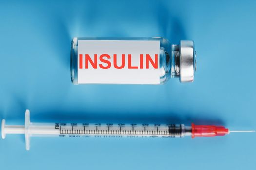 A bottle of insulin hormone and a syringe on the table on a blue background