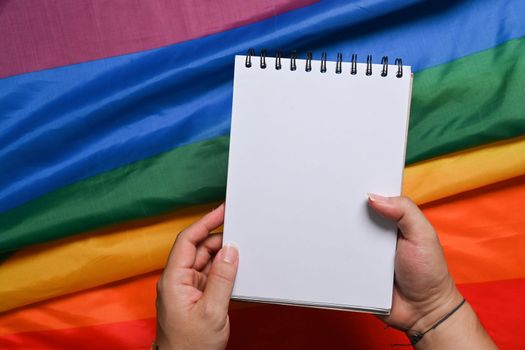 Man holding empty notepad over colorful LGBT rainbow flag.
