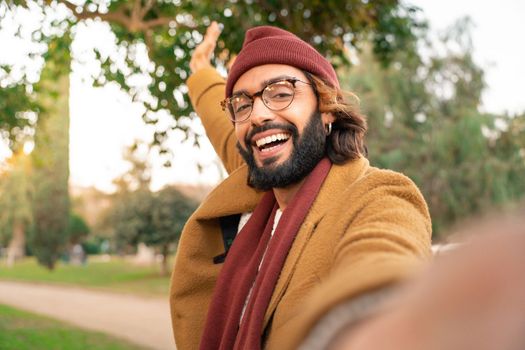Happy young caucasian man with glasses and beard taking a selfie outdoors in the park in winter. Happy smiling student video call. Technology and communication concept.