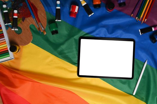 Digital tablet and artist tools over colorful rainbow flag.