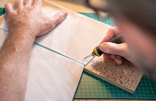 Closeup of a man working with pyrographer burning the wood making artwork craft at home art studio. High quality photo