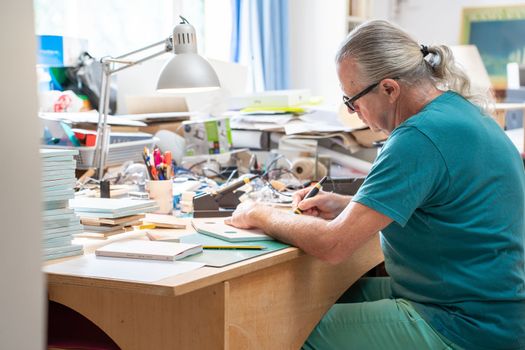 Creative mature man working with pyrographer burning the wood making artwork craft at home art studio. High quality photo