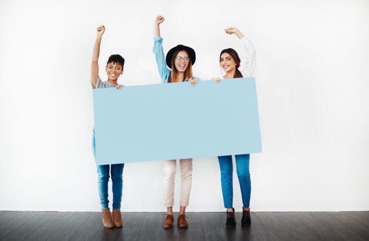 Shout out to women everywhere. Studio shot of a group of young women holding a blank placard and cheering against a white background