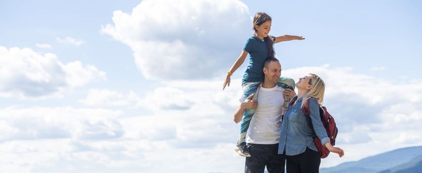 Family standing with arms around on top of mountain, looking at beautiful summer mountain landscape. People enjoying view