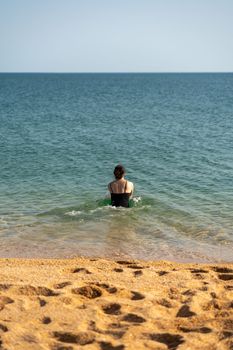 Woman sea swimsuit sand. The girl swims in the sea in a black swimsuit, the water is clean and transparent. Alone on the beach on a sunny day